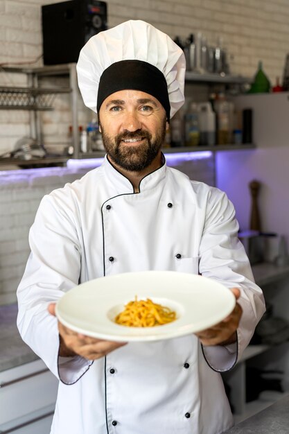 Portrait de chef masculin dans la cuisine tenant une assiette de nourriture