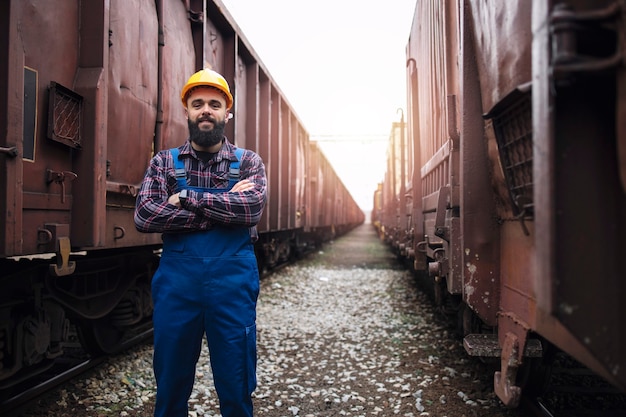 Portrait de cheminot avec les bras croisés debout fièrement à la gare entre les wagons