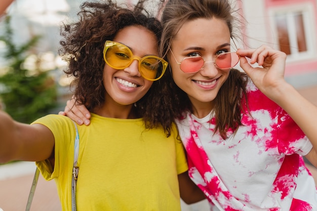 Portrait coloré d'amis heureux jeunes filles souriant assis dans la rue en prenant selfie photo sur téléphone mobile, les femmes s'amusant ensemble