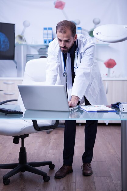 Portrait complet d'un beau médecin travaillant sur son ordinateur portable au cabinet de l'hôpital. Médecin dans un laboratoire.