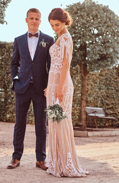 Portrait complet du corps de belles jeunes mariées - charmante mariée avec son beau marié posant dans le parc par une journée ensoleillée.