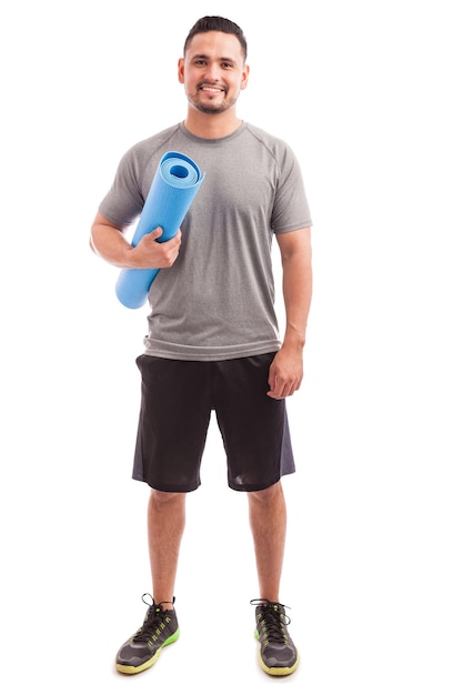 Portrait complet d'un jeune homme hispanique portant un tapis d'exercice prêt pour son cours de yoga