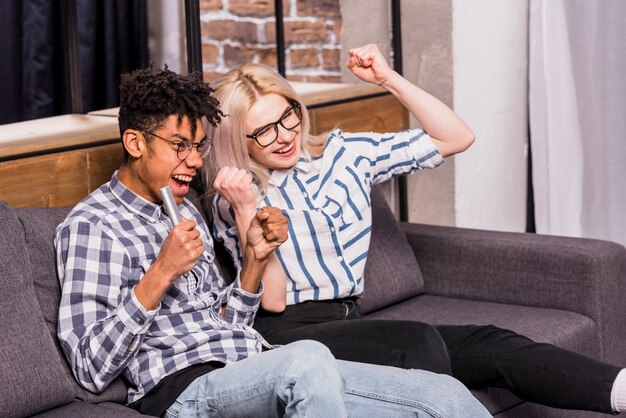 Portrait d&#39;un couple d&#39;adolescents excité assis sur un canapé, serrant leur poing