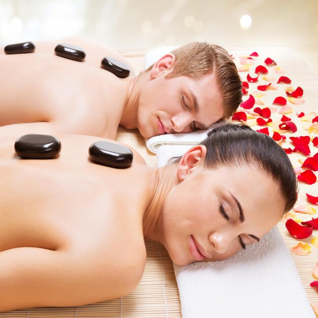Portrait de couple attrayant se détendre dans un salon spa avec des pierres chaudes sur le corps.