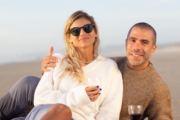 Portrait de couple au pique-nique au coucher du soleil. Homme et femme en vêtements décontractés assis et allongés sur le sable, regardant la caméra. Pique-nique, repas, concept d'amour