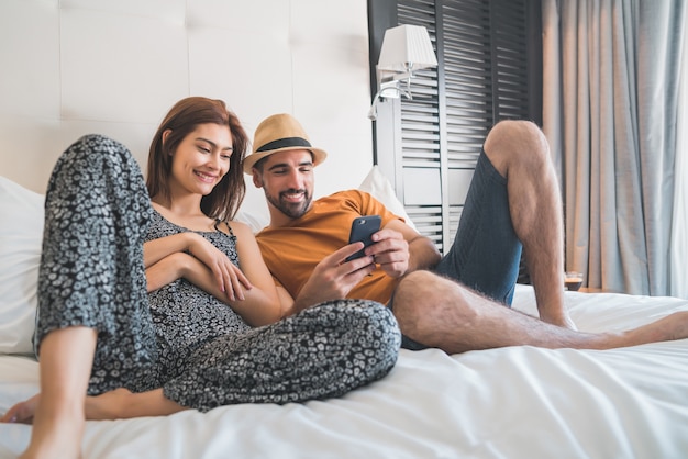 Portrait de couple charmant se détendre et à l'aide de téléphone portable en position couchée sur le lit à la chambre d'hôtel. Concept de mode de vie et de voyage.