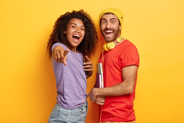 Portrait de couple élégant joyeux posant contre le mur jaune avec des gadgets