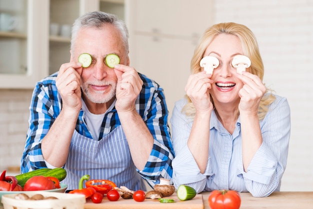 Portrait d&#39;un couple de personnes âgées couvrant leurs yeux avec des tranches de concombre et de champignons