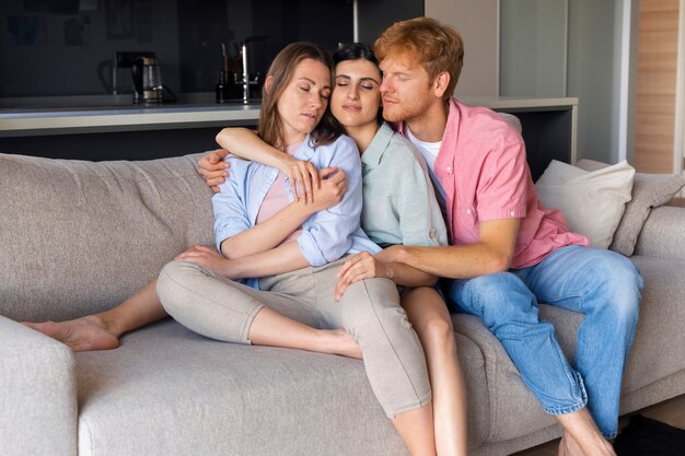 Portrait de couple polyamoureux à la maison assis sur le canapé ensemble