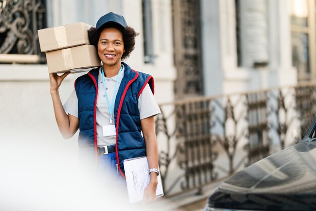 Portrait d'un courrier afro-américain heureux transportant des colis tout en effectuant une livraison dans la ville