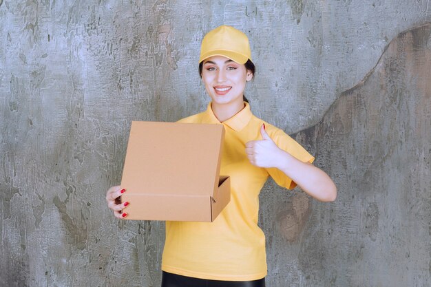 Portrait de courrier féminin tenant une boîte en carton et montrant le pouce vers le haut