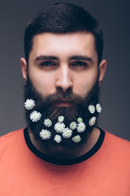 Portrait créatif du jeune bel homme avec une barbe décorée de fleurs.