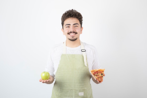 Portrait d'un cuisinier masculin souriant montrant une pizza et une pomme verte sur blanc