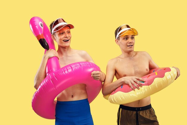 Portrait demi-longueur de deux jeunes hommes isolés. Amis souriants en casquettes avec anneaux de bain. Expression faciale, concept d'été, de week-end, de villégiature ou de vacances. Couleurs à la mode.