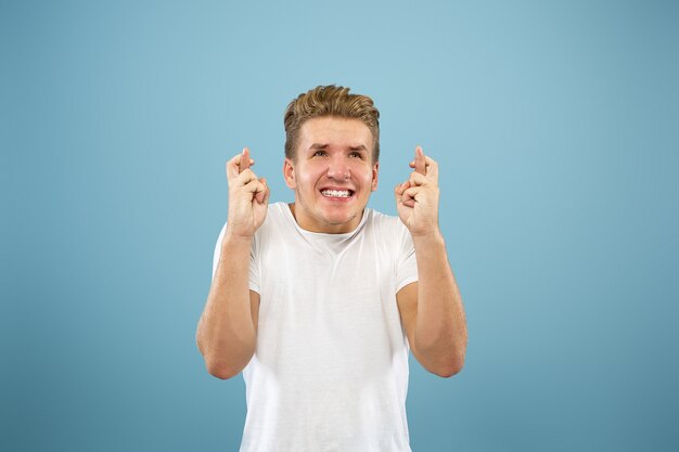 Portrait demi-longueur du jeune homme caucasien sur fond bleu studio. Beau modèle masculin en chemise. Concept d'émotions humaines, expression faciale, ventes, publicité. Montrant un geste de bonne chance.