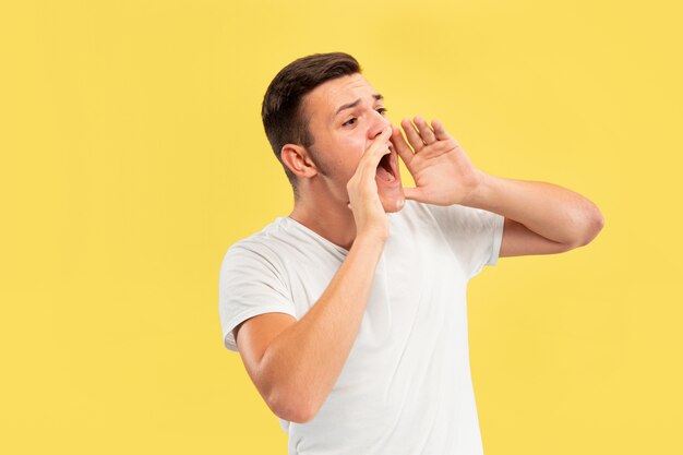 Portrait demi-longueur du jeune homme caucasien sur fond de studio jaune. Beau modèle masculin en chemise. Concept d'émotions humaines, expression faciale, ventes, publicité. Appeler quelqu'un, copyspace.