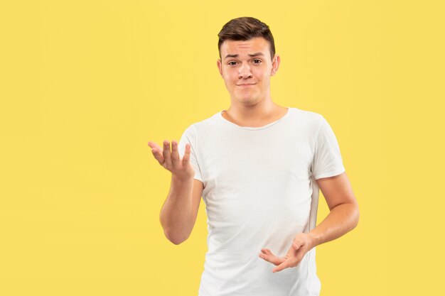 Portrait demi-longueur du jeune homme caucasien sur fond de studio jaune. Beau modèle masculin en chemise. Concept d'émotions humaines, expression faciale, ventes, publicité. Pointant et montrant quelque chose.