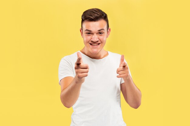 Portrait demi-longueur du jeune homme caucasien sur fond de studio jaune. Beau modèle masculin en chemise. Concept d'émotions humaines, expression faciale, ventes, publicité. Pointant et semble heureux.