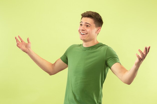 Portrait demi-longueur du jeune homme caucasien sur fond vert studio. Beau modèle masculin en chemise. Concept d'émotions humaines, expression faciale, ventes, publicité. Sourire, saluer, inviter.