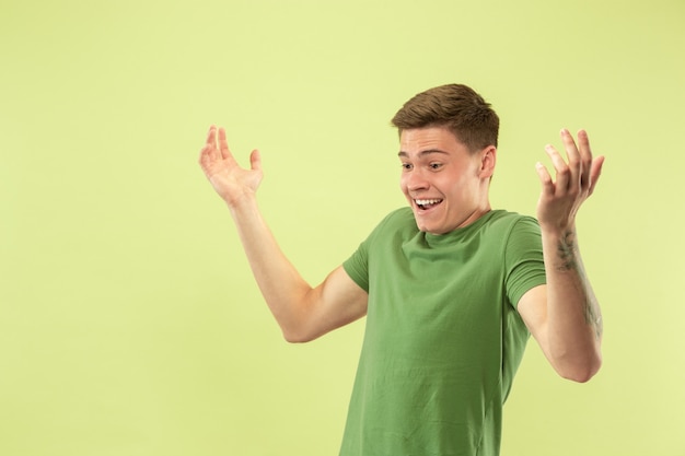 Portrait demi-longueur du jeune homme caucasien sur fond vert studio. Beau modèle masculin en chemise. Concept d'émotions humaines, expression faciale, ventes, publicité. Étonné, choqué, interrogé.