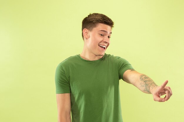 Portrait demi-longueur du jeune homme caucasien sur fond vert studio. Beau modèle masculin en chemise. Concept d'émotions humaines, expression faciale, ventes, publicité. Toucher la barre de recherche d'espace vide.