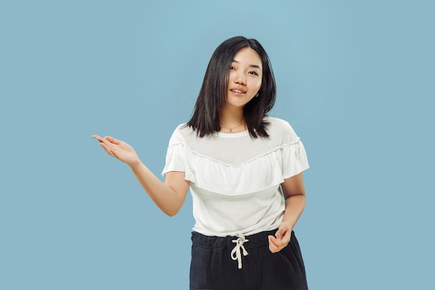 Portrait demi-longueur de la jeune femme coréenne sur l'espace bleu. Modèle féminin en chemise blanche. Montrer et pointer quelque chose.