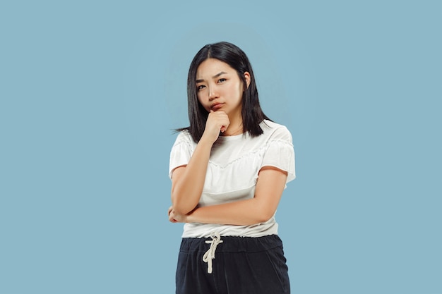 Portrait demi-longueur de la jeune femme coréenne sur l'espace bleu. Modèle féminin en chemise blanche. Réfléchi, semble sérieux.