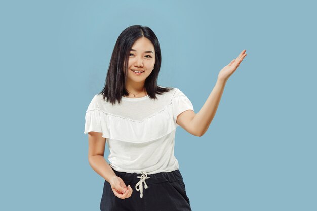 Portrait demi-longueur de la jeune femme coréenne. Modèle féminin en chemise blanche. Montrer et pointer quelque chose. Concept d'émotions humaines, expression faciale. Vue de face.