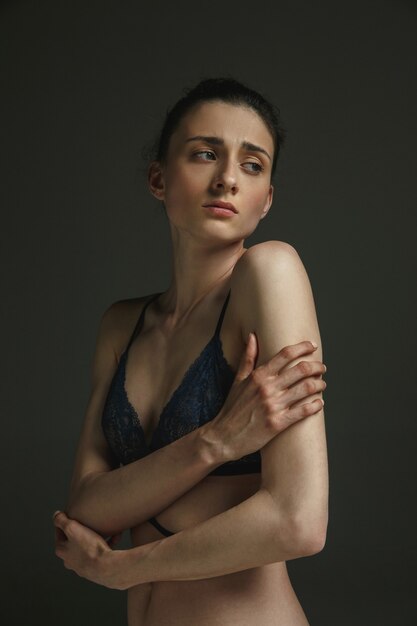 Portrait demi-longueur de jeune femme triste en sous-vêtements sur un mur de studio sombre