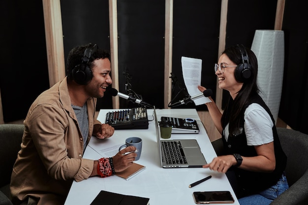 Portrait de deux animateurs de radio joyeux, jeune homme et femme riant tout en discutant de divers sujets