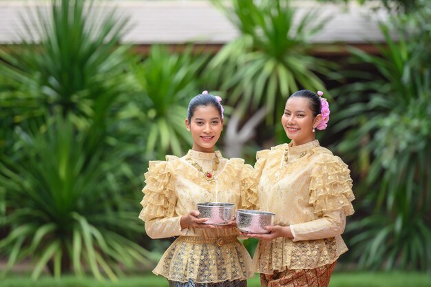 Portrait de deux belles femmes au festival de Songkran avec costume traditionnel thaïlandais dans le temple tenant un bol d'eau et souriant Culture thaïlandaise avec festival de l'eau