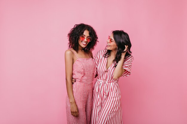 Portrait de deux filles africaines émotionnelles joyeuses aux cheveux bouclés. Les sœurs en robes d'été rayées se réjouissent.