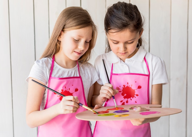 Photo gratuite portrait de deux filles à l'aide d'une palette pour peindre avec un pinceau