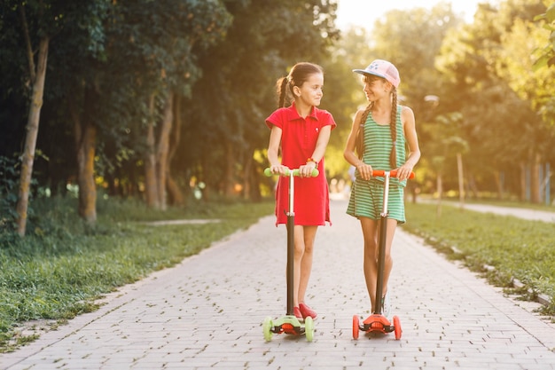 Portrait, deux, filles, debout, pousser, scooter, regarder, autre