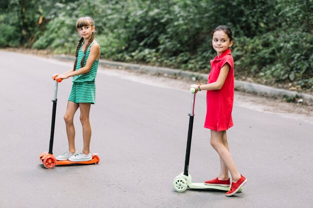 Portrait, deux, filles, debout, pousser, scooter, rue