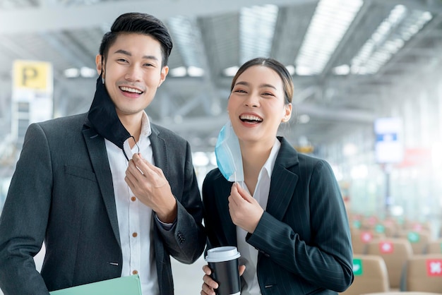 Portrait de deux hommes d'affaires asiatiques portant un masque facial contre le virus protégeant le sourire avec accueil et confiance regardant la caméra avec arrière-plan flou du terminal de l'aéroport distanciation sociale nouveau mode de vie normal