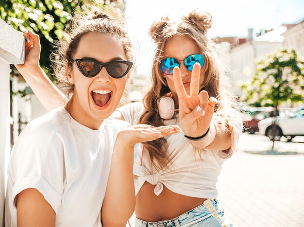 Portrait de deux jeunes belles femmes hipster souriantes dans des vêtements de t-shirt blanc d'été à la mode