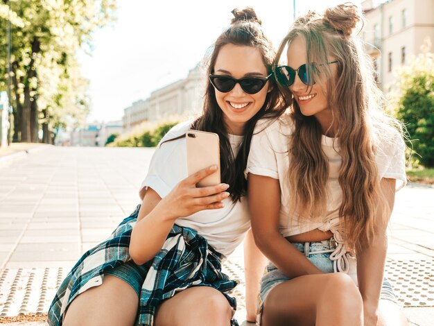 Portrait de deux jeunes belles femmes hipster souriantes dans des vêtements de t-shirt blanc d'été à la mode