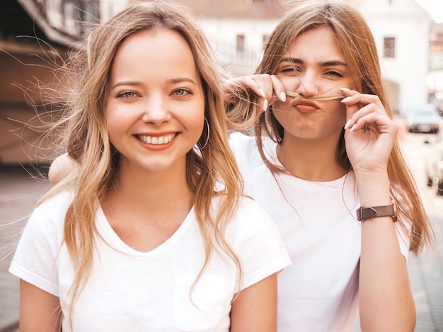 Portrait de deux jeunes belles filles blondes souriantes hipster dans des vêtements de t-shirt blanc à la mode d'été. . Modèles positifs s'amusant