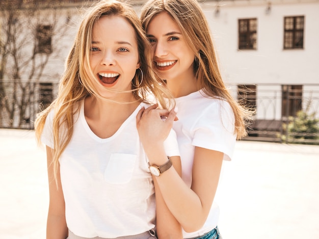 Portrait de deux jeunes belles filles blondes souriantes hipster dans des vêtements de t-shirt blanc à la mode d'été. . Modèles positifs s'amusant.