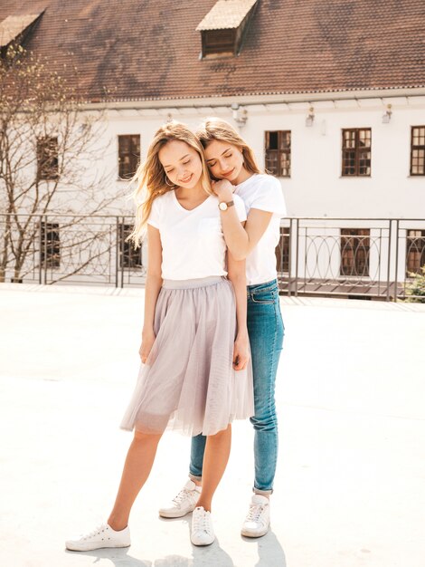 Portrait de deux jeunes belles filles blondes souriantes hipster dans des vêtements de t-shirt blanc à la mode d'été. . Modèles positifs s'amusant.