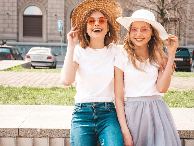 Portrait de deux jeunes belles filles blondes souriantes hipster dans des vêtements de t-shirt blanc à la mode d'été.