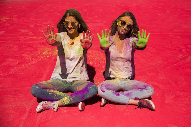 Photo gratuite portrait de deux jeunes femmes montrant leurs paumes peintes en couleur holi