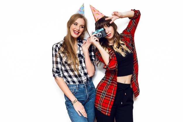 Portrait de deux jolies femmes posant sur un mur blanc avec des chapeaux de fête