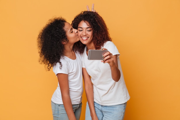 Portrait de deux soeurs afro-américaines heureux prenant selfie avec smartphone, baiser mignon