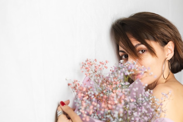 Portrait doux d'une jeune femme sur un chiffon blanc topless tenant un bouquet de fleurs multicolores sèches et souriant mignon, anticipation du printemps