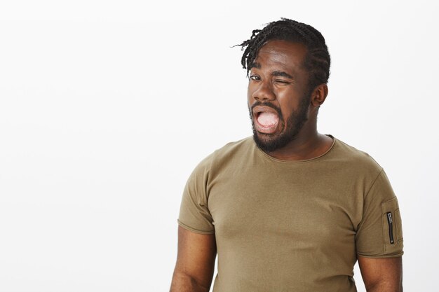 Portrait de drôle de gars intrigant dans un t-shirt marron posant contre le mur blanc