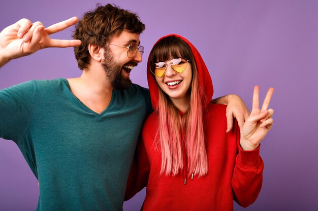 Portrait drôle positif de couple heureux s'amuser ensemble, câlins et rire, famille et amour, vêtements et accessoires de jeunesse décontractés, montrant le geste de paix