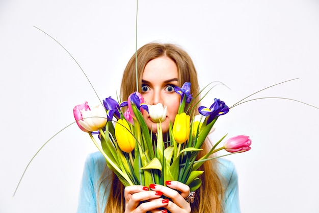 Portrait drôle de studio de femme blonde ferme son visage par beau bouquet de tulipes colorées, couleurs pastel tendres, robe vintage, poils longs, détails de mode. le printemps arrive