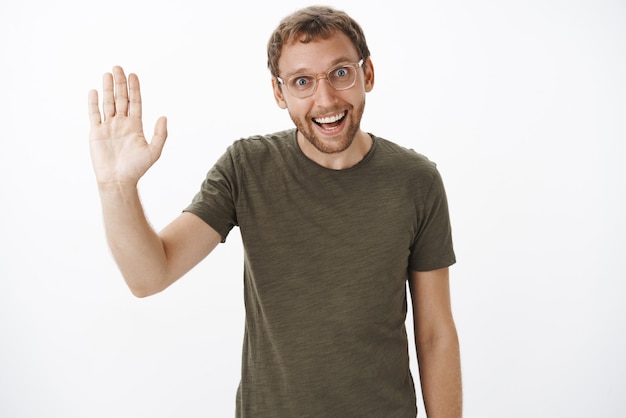 Photo gratuite portrait de drôle de type caucasien mal rasé enthousiaste en t-shirt vert foncé et lunettes transparentes soulevant la paume et disant bonjour